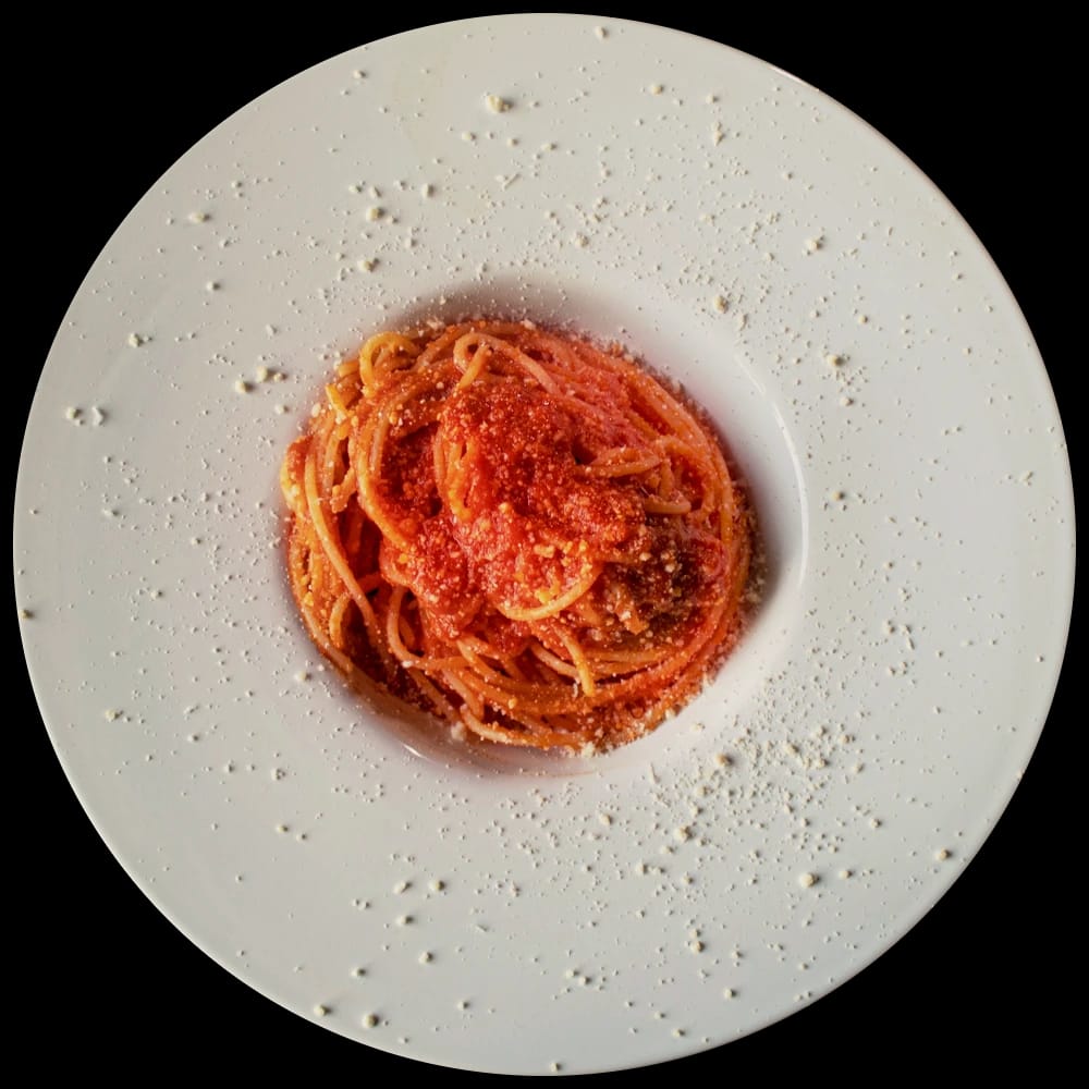 Ninho de espaguete ao molho de tomate com queijo ralado, no centro de um prato fundo branco de aba larga, visto de cima